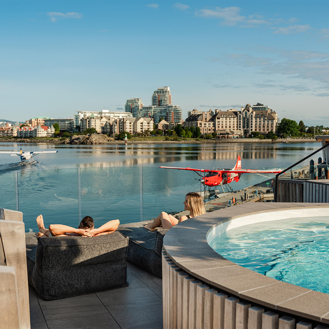 A couple sun bathes on the deck at HAVN Saunas watching the seaplanes at they take off from the Inner Harbour in Victoria, BC